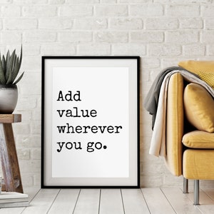 Puede incluir: Impresión tipográfica en blanco y negro en un marco negro con el texto "Add value wherever you go." La impresión está colgada en una pared de ladrillo blanco sobre un sofá amarillo.