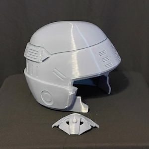Könnte beinhalten: Ein grauer 3D-gedruckter Helm mit Visier und einem separaten, ebenfalls 3D-gedruckten Gesichtsvisier.