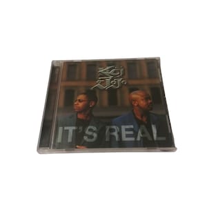 May include: A CD case with a black and white photo of two men in front of a brick building. The text "K-Ci & JoJo" is in silver lettering at the top of the case. The text "IT'S REAL" is in white lettering at the bottom of the case.