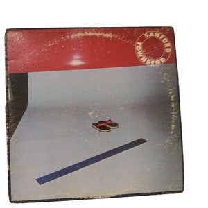 May include: A red and blue album cover with the text "Sanford Townsend" in a circle. The cover features a blue line and a pair of red and black sandals on a light blue background.