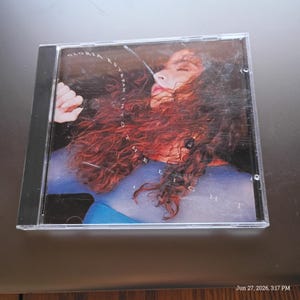May include: A compact disc in a clear plastic jewel case featuring the album Into the Light by Gloria Estefan. The cover art displays a portrait of a person with long, wavy reddish-brown hair wearing a blue top, with the text Gloria Estefan Into the Light printed in white.