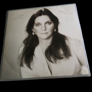 May include: A vintage vinyl record album cover featuring a black and white photo of Judy Collins. The album title is "Bread and Roses" and is printed in white text on a light gray background.