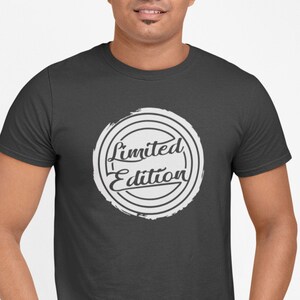 Könnte beinhalten: Ein dunkelgraues T-Shirt mit einem weißen Kreis-Motiv, auf dem in einer stilisierten Schrift "Limited Edition" steht.