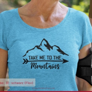 Könnte beinhalten: Ein hellblaues T-Shirt mit einer schwarzen Berggrafik und dem Text "Take Me To The Mountains" mit einem Pfeil, der nach rechts zeigt.