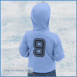 Könnte beinhalten: Ein hellblauer Kapuzenpullover mit einer schwarzen Nummer 9 auf der Rückseite. Der Text "Farbe: 31 - schwarz (Flex)" ist am unteren Rand des Bildes gedruckt.