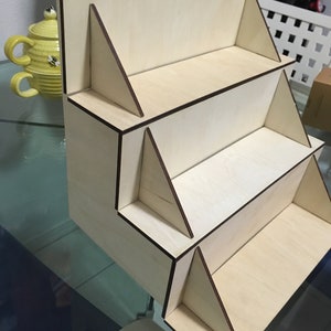 May include: A wooden display stand with four shelves. The stand is made of light wood with dark brown edges. The shelves are all the same size and are evenly spaced.
