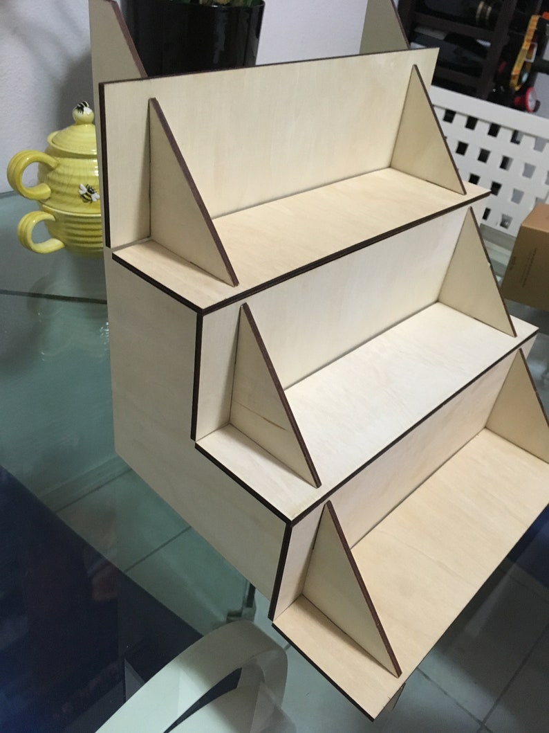 May include: A wooden display stand with four shelves. The stand is made of light wood with dark brown edges. The shelves are all the same size and are evenly spaced.
