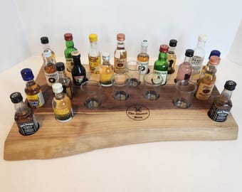 Puede incluir: Una bandeja de servir de madera con un acabado de madera natural y un recorte para vasos de chupito. La bandeja está llena de botellas de licor en miniatura, incluyendo Absolut Mandarin, Jack Daniels y Jameson. La bandeja está grabada con el texto "Chris Schwenkeritz Board".