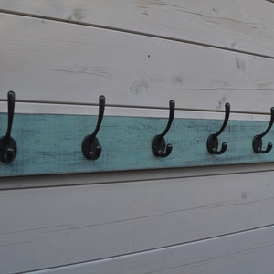 May include: A rustic wooden coat rack with six black metal hooks. The wood is painted a light blue-green colour and has a distressed finish.