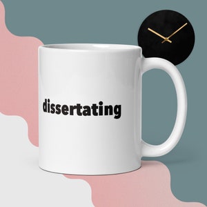 Op de afbeelding: Witte keramische koffiemok met het woord "dissertating" in het zwart op de voorkant.