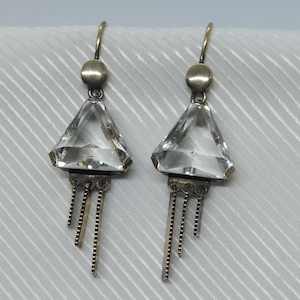 Könnte beinhalten: Ein Paar Vintage-Ohrringe mit klaren, facettierten, dreieckigen Kristallen. Die Kristalle sind in einem silberfarbenen Metall mit einem kleinen, runden Akzent oben und hängenden Kettendetails unten gefasst. Die Ohrringe haben einen Hakenverschluss.