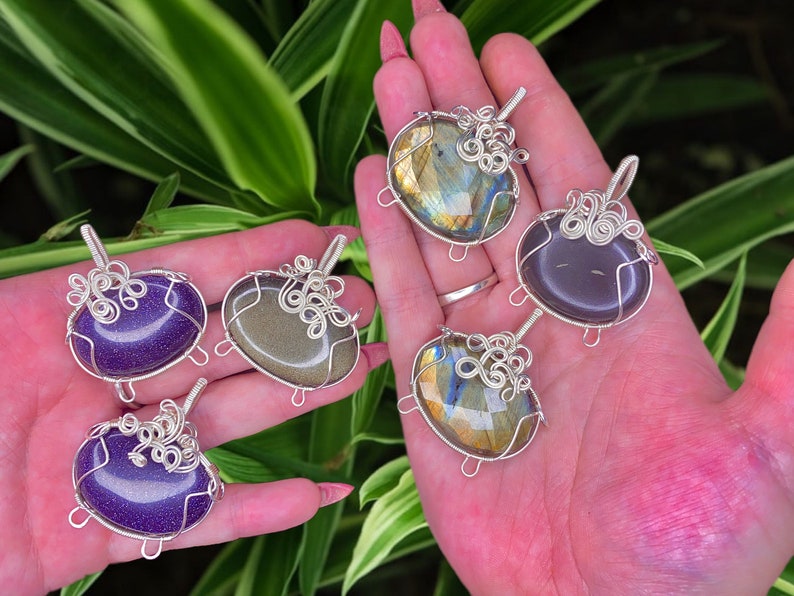 May include: Five wire-wrapped pendants with different colored stones. The stones are a purple, green, gray, and two iridescent blue stones. The wire is silver.