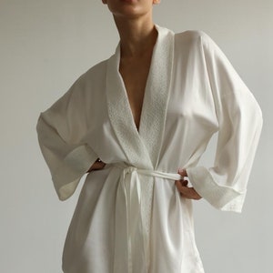 May include: A white satin robe with a lace trim around the collar and cuffs. The robe has a sash tie at the waist.