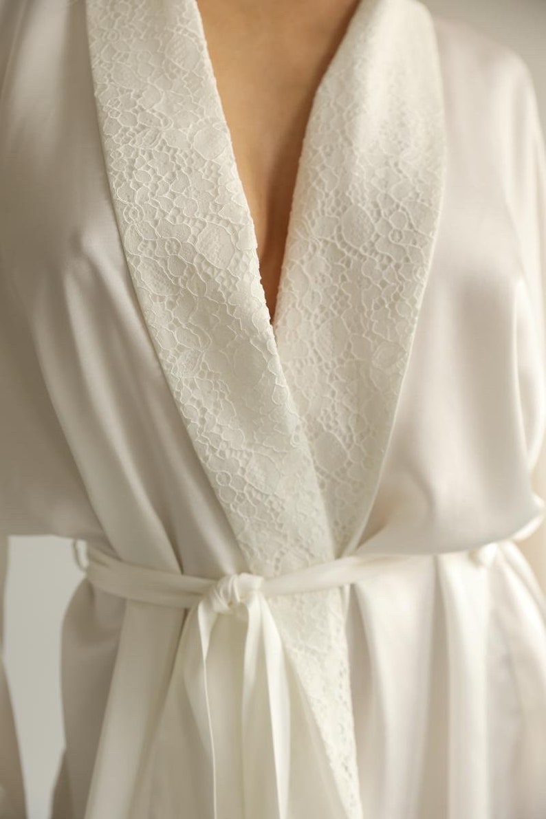 May include: A white satin robe with a lace trim around the collar and a matching tie belt.