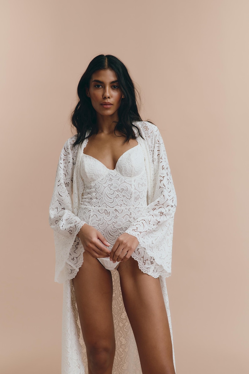 May include: A white lace robe with long sleeves and a deep V-neckline. The robe is made of delicate lace and has a flowing silhouette.