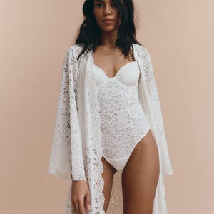 May include: A white lace robe with long sleeves and a deep V-neckline. The robe is made of delicate lace and has a flowing silhouette.
