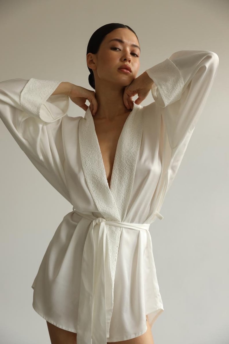 May include: A white satin robe with a lace trim collar and tie. The robe has long sleeves and a relaxed fit.