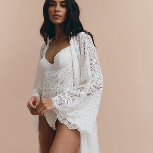 May include: A white lace robe with long sleeves and a flowing hem. The robe is made of delicate lace and has a feminine and romantic look.