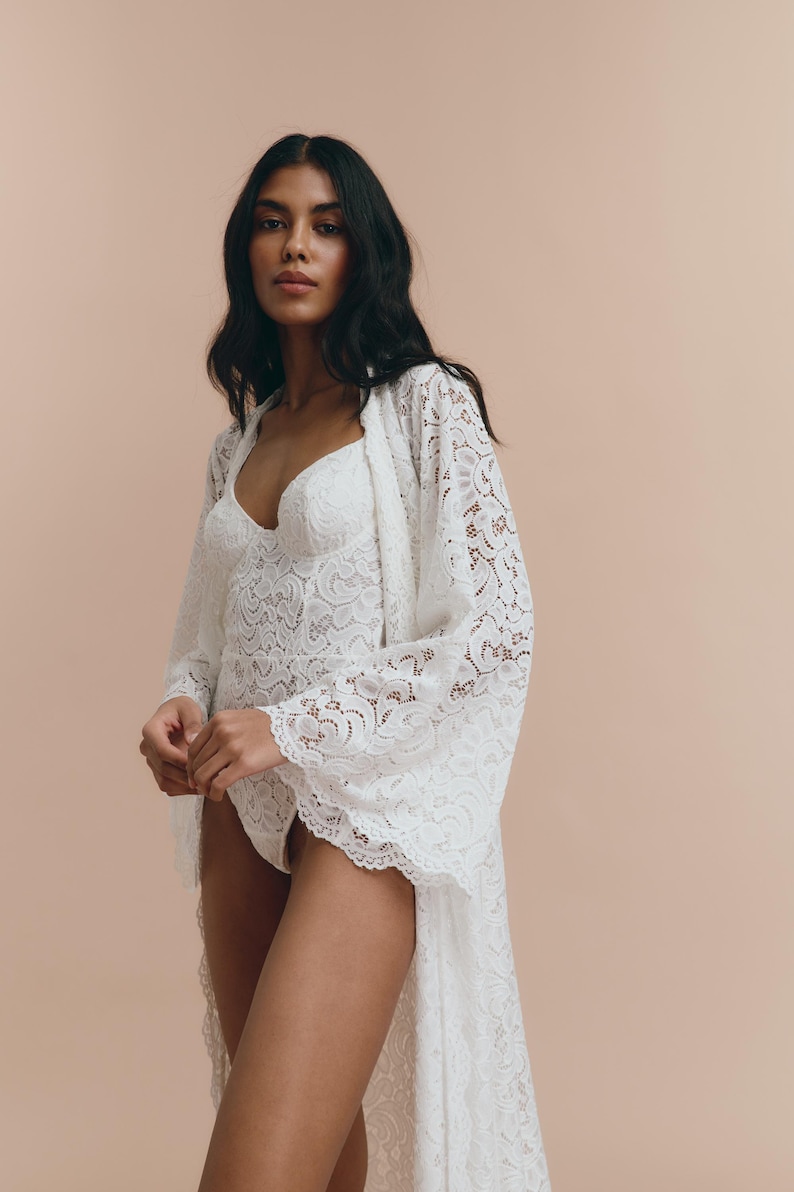 May include: A white lace robe with long sleeves and a flowing hem. The robe is made of delicate lace and has a feminine and romantic look.