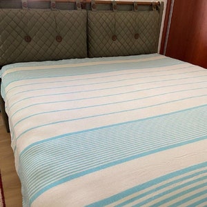 Könnte beinhalten: Eine weiße und hellblaue gestreifte Wolldecke mit Fransen. Die Decke liegt auf einem Bett mit einem grünen Kopfteil.