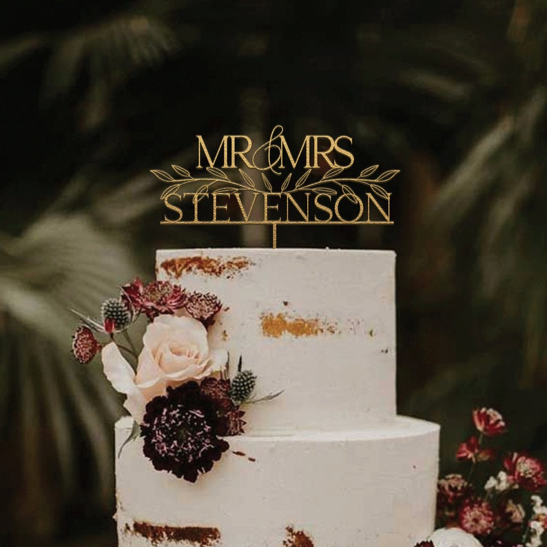 May include: A gold wedding cake topper with the text "MR & MRS STEVENSON" and a leafy design.