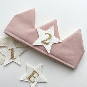 May include: A pink felt crown with a white felt star with a gold glitter number "2" on it. There are two additional white felt stars with gold glitter letters "1" and "E" on them.