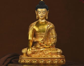 May include: A golden Buddha statue in a seated position, with intricate detailing on the robe and base. The statue has a serene expression and a black, textured hairstyle. The background is a warm brown with a hint of red floral accents.