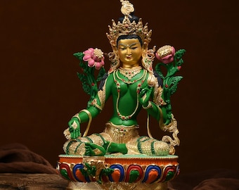 May include: A detailed statue of a seated deity, featuring a green body, gold accents, and a jeweled crown. The figure holds lotus flowers and is adorned with intricate jewelry. The base is decorated with colorful patterns.