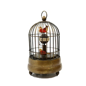 May include: A brass birdcage clock with three red birds inside. The clock face is visible through the cage and has Roman numerals.