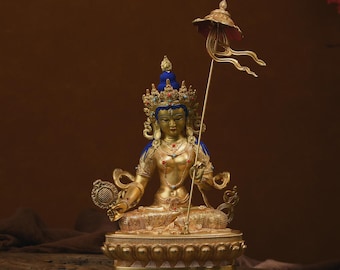 May include: A gold-coloured statue of a deity with a blue crown and a blue and gold umbrella. The statue is sitting on a lotus-shaped base.