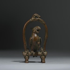 May include: A bronze parrot sculpture perched on a bamboo-style frame. The bird has an open beak and is surrounded by a decorative arch. The base features rope-like detailing, and the overall design is detailed and ornate.