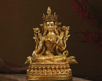 May include: A gold-coloured statue of a seated deity with a serene expression, wearing an ornate crown and jewellery. The figure is positioned in a cross-legged pose on a lotus-shaped base, featuring intricate carvings and delicate floral accents.