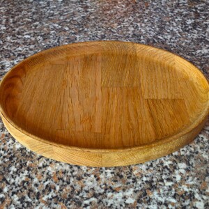 Op de afbeelding: Een ronde houten serveerschaal met een natuurlijke houten afwerking. De schaal is gemaakt van houten planken en heeft een licht verhoogde rand.