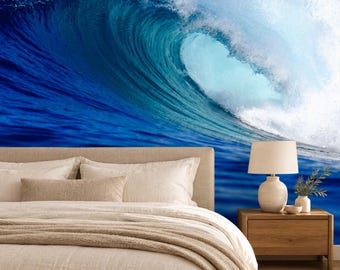 May include: A bedroom featuring a wall mural of a large, crashing ocean wave in shades of deep blue and white. The bed has a beige upholstered headboard, light-colored bedding, and a textured throw blanket. A wooden nightstand holds a lamp.