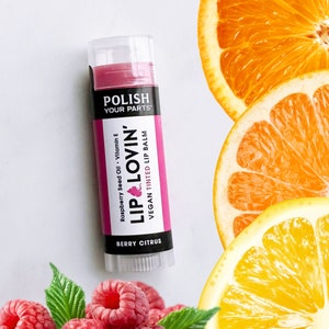 May include: A pink vegan tinted lip balm tube with the words "POLISH YOUR PARTS" and "LIP LOVIN'" in black text. The tube also says "Raspberry Seed Oil - Vitamin E" and "BERRY CITRUS".
