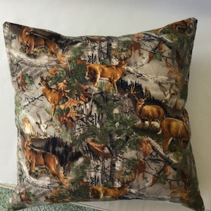 May include: A brown and tan throw pillow with a camouflage pattern featuring deer and trees.
