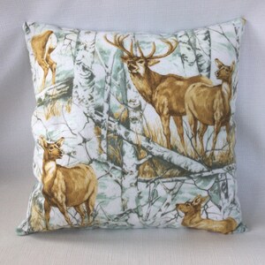 May include: A decorative throw pillow with a white background and a camouflage pattern featuring brown deer in a forest setting.