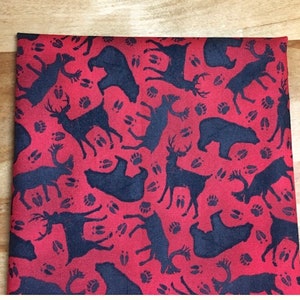 May include: Red fabric with a repeating pattern of black silhouettes of deer, bears, and paw prints.
