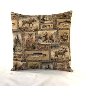 May include: A brown and beige throw pillow with a tapestry-like design featuring a variety of woodland animals, including owls, moose, bears, and fish. The pillow is made up of a patchwork of different scenes, each with a different animal or plant.