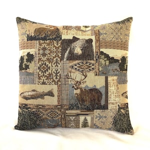 May include: A square throw pillow with a tapestry-style design featuring a patchwork of images including a deer, a bear, a fish, and trees. The background is a mix of brown, beige, and blue.