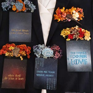 May include: A black suit jacket with five small cards pinned to it. The cards have different designs and text, including "Will Beyond Measure", "Where Dwell The Brave At Heart", "Show Me Your Brave Heart", and "The Things I Do For Love". The jacket also has a small 3D printed logo that says "Darth Vinci 3D".