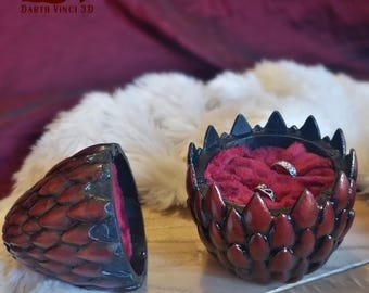 May include: A two-piece ring box shaped like a dragon egg with a dark red and black scale texture. The interior is lined with deep red velvet, holding two silver rings. The lid is detached, and the text "3DV DARTH VINCI 3D" appears in the corner.