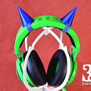 May include: Green gaming headphones with blue horns on top. The headphones are on a white stand. The text "Z.V" is on the headband.
