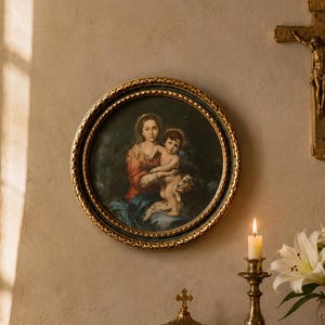 Può includere: Una natura morta religiosa con un dipinto incorniciato di Maria e Gesù, un crocifisso, una candela accesa in un portacandele di ottone, un rosario, un libro e un vaso di gigli bianchi. Gli oggetti sono disposti su un tavolo con piano in marmo.