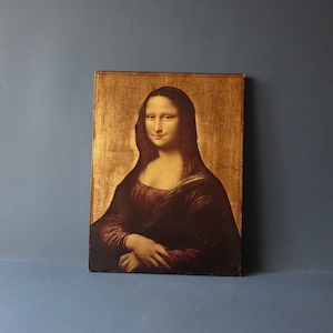 Puede incluir: Una impresión enmarcada de la pintura de la Mona Lisa. La pintura tiene un fondo dorado y la mujer en la pintura lleva un vestido oscuro y tiene una sonrisa suave.