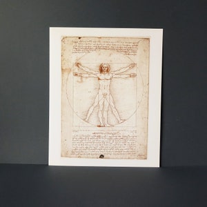 May include: A black and white print of a drawing of a nude male figure in a circle and square. The figure is in a pose with arms outstretched and legs spread apart. The drawing is titled "Vitruvian Man" and is attributed to Leonardo da Vinci.