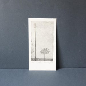 May include: Monochrome print of a street lamp and a tree. The artwork is on a white rectangular card. The print has a minimalist style with fine lines and a textured appearance. The background is a light gray.