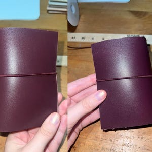 May include: A burgundy leather journal with an elastic closure. The rectangular journal has rounded corners. An elastic band wraps around it to keep it closed. The journal is displayed on a wooden surface.