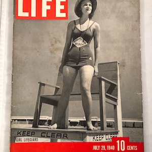 May include: A black and white photo of a woman in a swimsuit standing on a lifeguard stand. She is wearing a hat and a lifeguard badge that says "Manhattan Beach". The stand has a sign that says "Keep Clear Girl Lifeguard". The magazine cover is for LIFE magazine, July 29, 1940, and costs 10 cents.