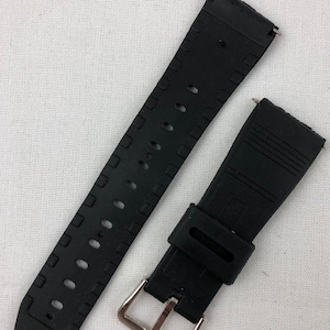 Puede incluir: Correa de reloj de goma negra con hebilla plateada. La correa tiene una superficie texturizada y est&aacute; dise&ntilde;ada para un reloj de pulsera.